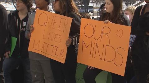 "Emotional day at the capital." A crowd stands holding orange signs which read "Queer lives matter" and "Our minds."