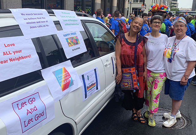 Marianne Graham, Kathleen Olsen, and Cheryl Maloney stand beside a van with several posters across its side.